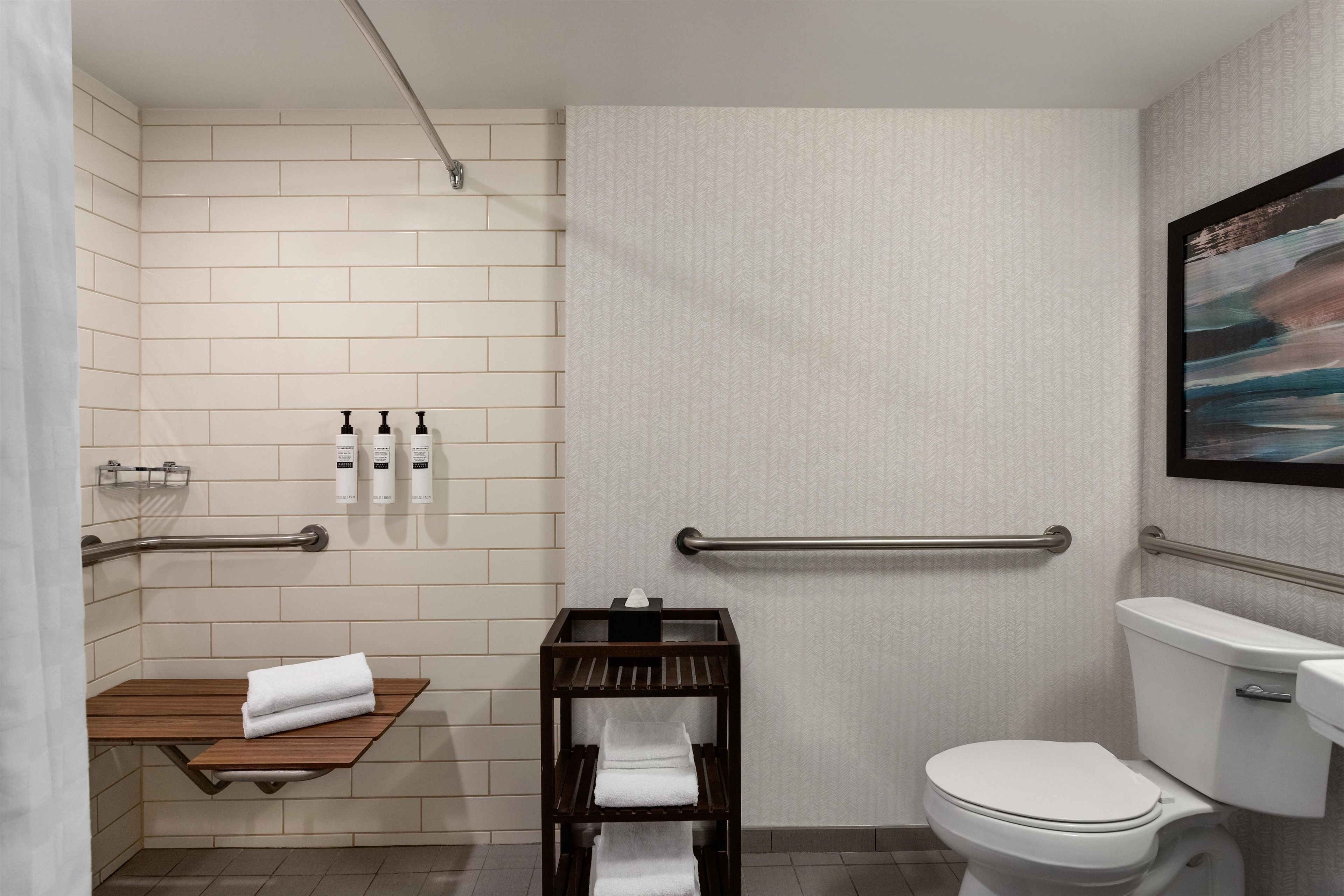 Un baño moderno con inodoro, un estante de madera con toallas, un pasamanos y un dispensador de toallas en la pared.