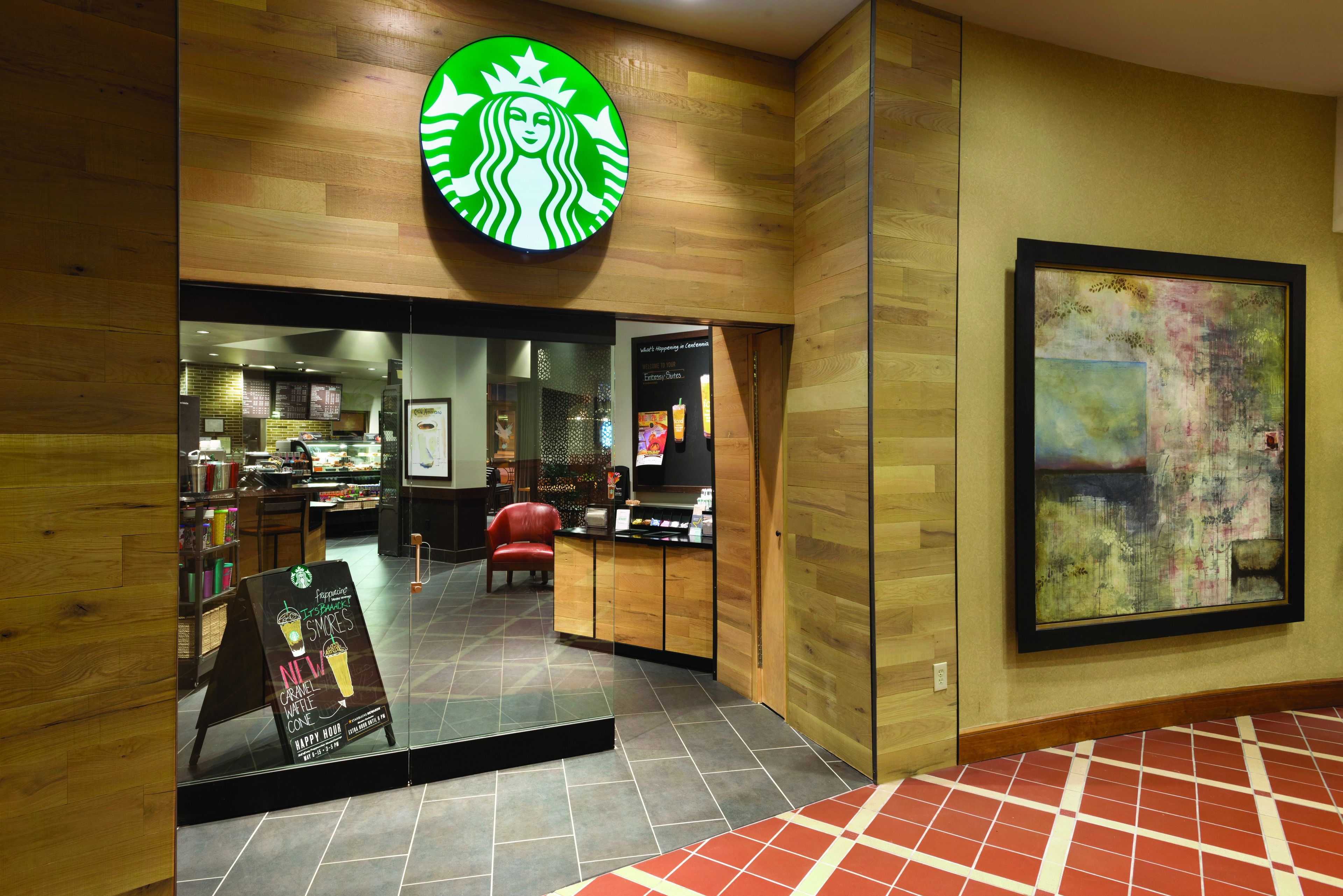 A Starbucks with a wooden interior, a red chair, and a framed abstract painting on the wall.