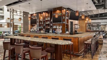 A bar area with a granite countertop, multiple stools, and a variety of bottles and glasses on shelves.