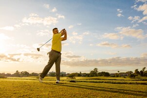 Un campo de golf con un jugador de camisa amarilla y pantalones caqui balanceando un palo de golf.