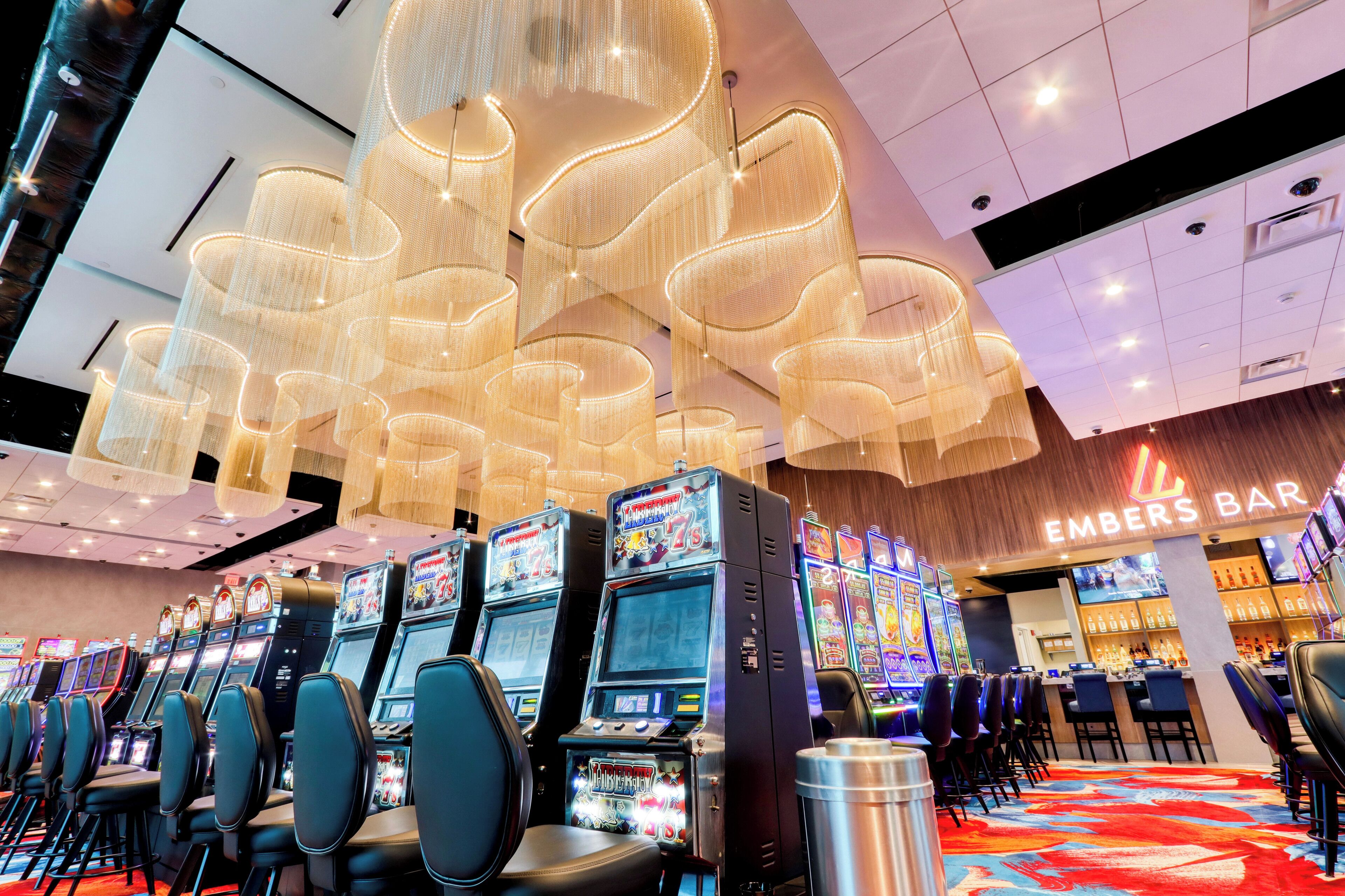 A casino area with slot machines, a bar named 'EMBERS BAR,' and a chandelier with a unique design.