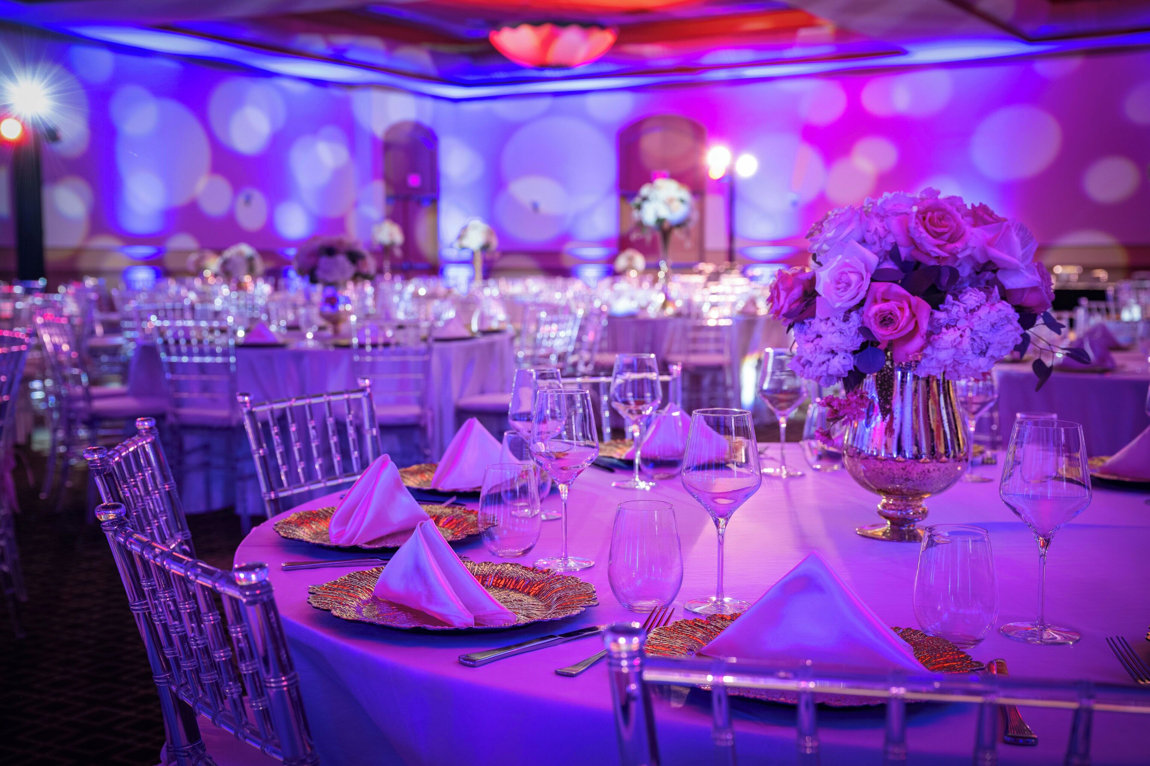 A banquet hall with round tables, chairs, and a central floral arrangement.
