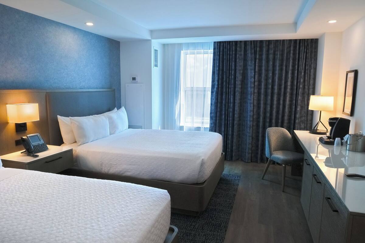 A hotel room with two beds, a desk with a chair, a phone, and a lamp.