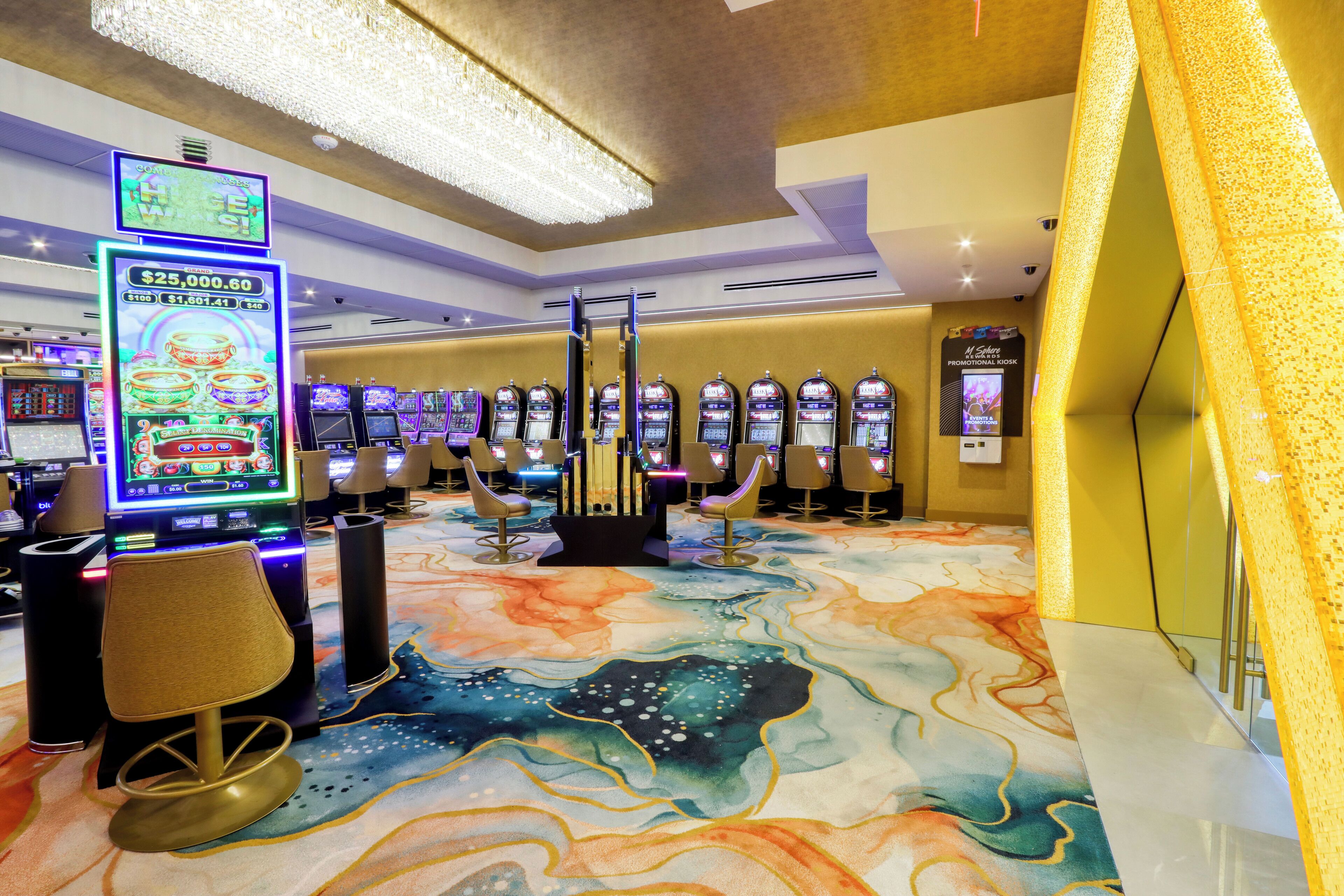 A casino floor with slot machines, a large chandelier, and a colorful carpet.