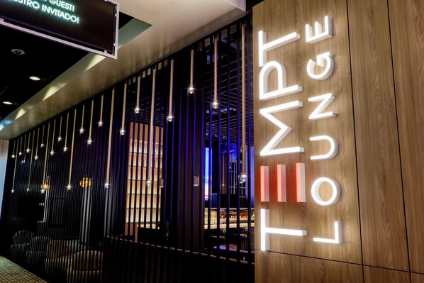 A hotel entrance with a sign reading "TEMPT LOUNGE" and a digital sign above stating "GUEST INVITED!".