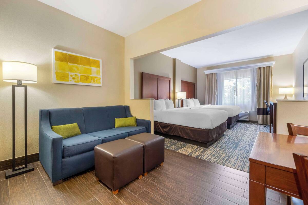 A hotel room with a bed, a sofa, a coffee table, a desk, and a lamp.
