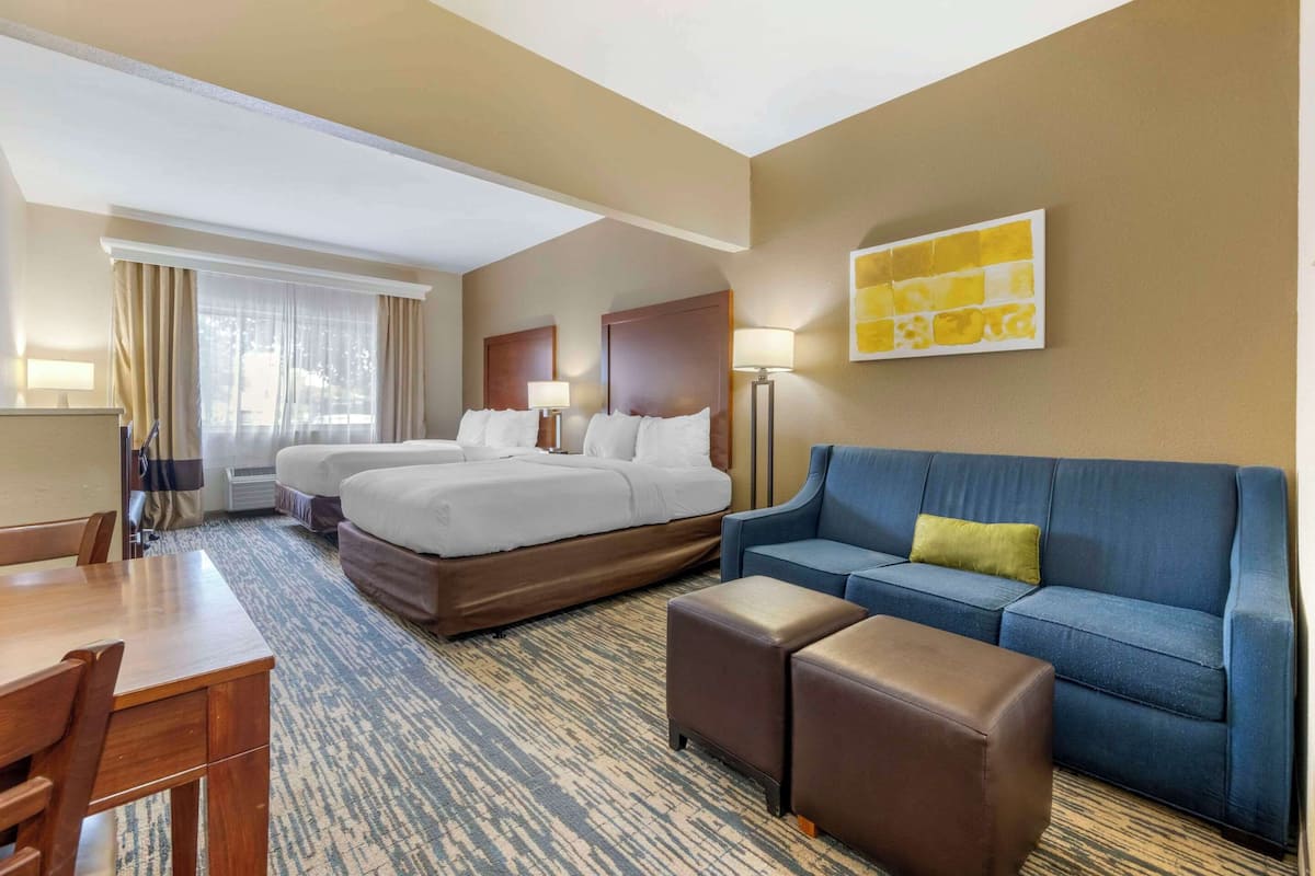 A hotel room with two beds, a blue sofa, a wooden desk, and a carpeted floor.