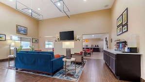 A hotel lobby with a blue sofa, a small table, a TV, and a kitchen area in the background. - Comfort Suites Keeneland (Lexington)