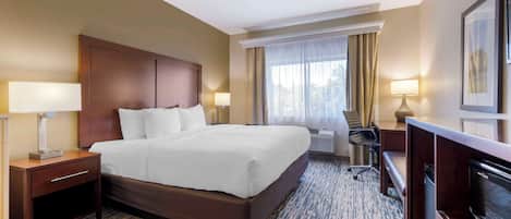 Una habitación de hotel con una cama grande, un escritorio, una silla, un televisor y un ventanal con cortinas.