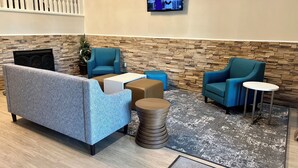 A lobby with a sofa, two armchairs, a coffee table, a small rug, and a television on the wall. - Clarion Suites Anchorage Downtown (Anchorage)
