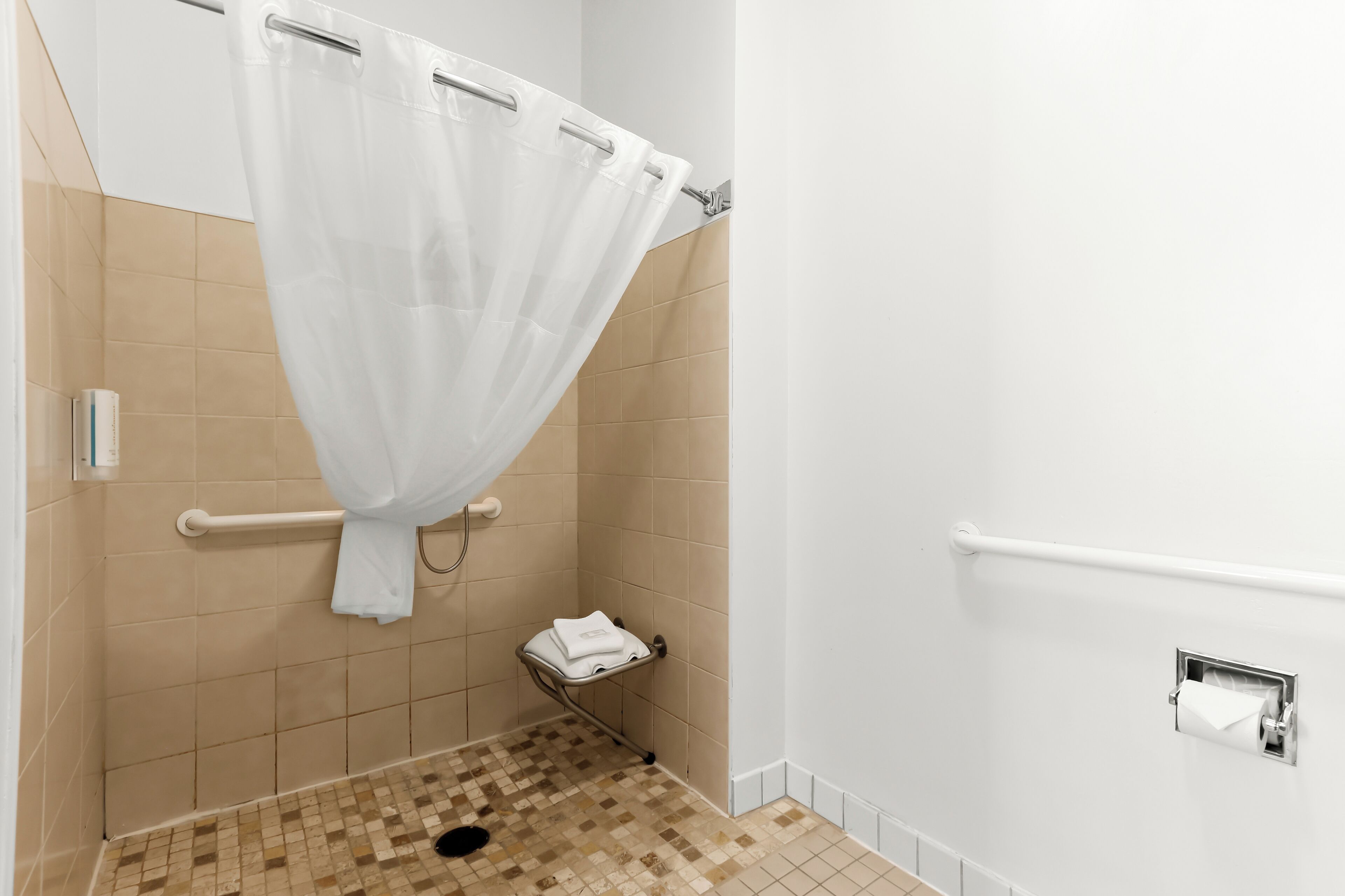 A bathroom with a shower curtain, a towel rack, a grab bar, and a toilet paper holder.