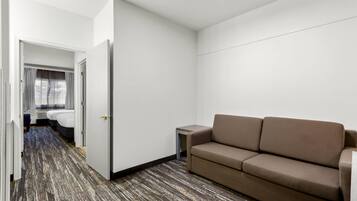 Una habitación de hotel con un sofá marrón, una mesita auxiliar pequeña y una alfombra estampada.