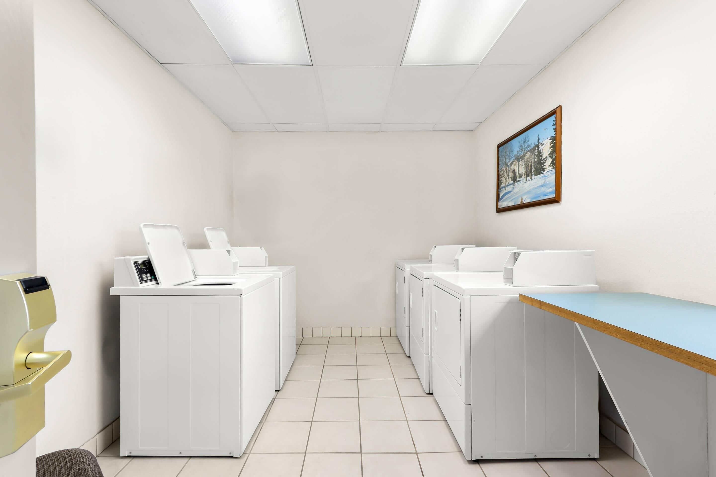 A laundry room with white appliances, a wooden counter, and a framed picture on the wall.