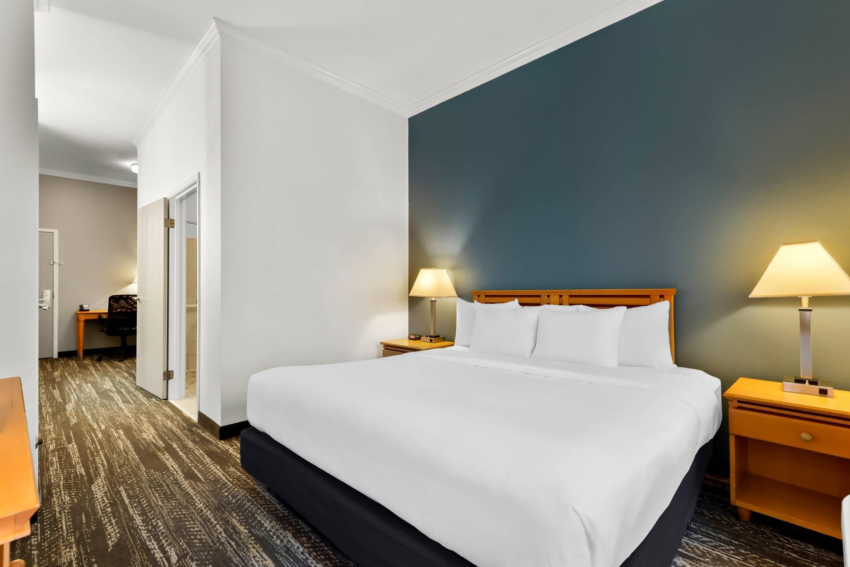 A hotel room with a large bed, two bedside tables with lamps, a wooden headboard, and a carpeted floor.