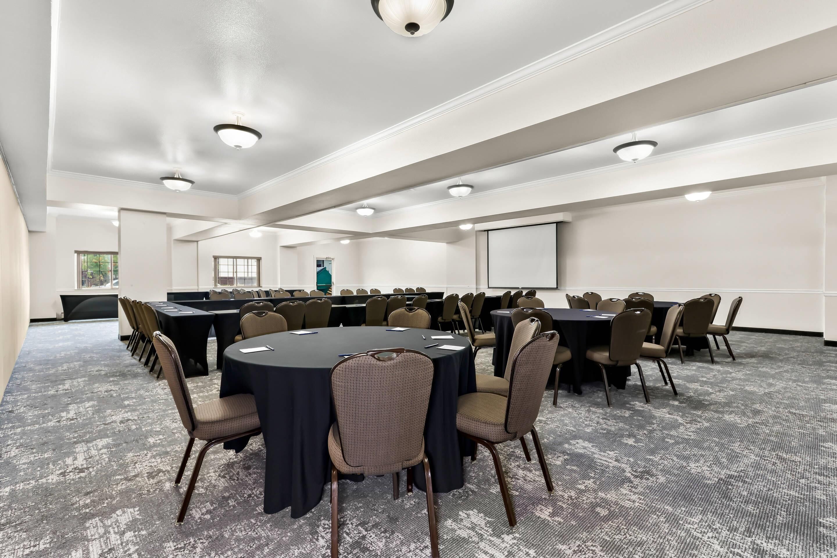 Une salle de conférence équipée de tables rondes, de chaises et d’un écran de projection.