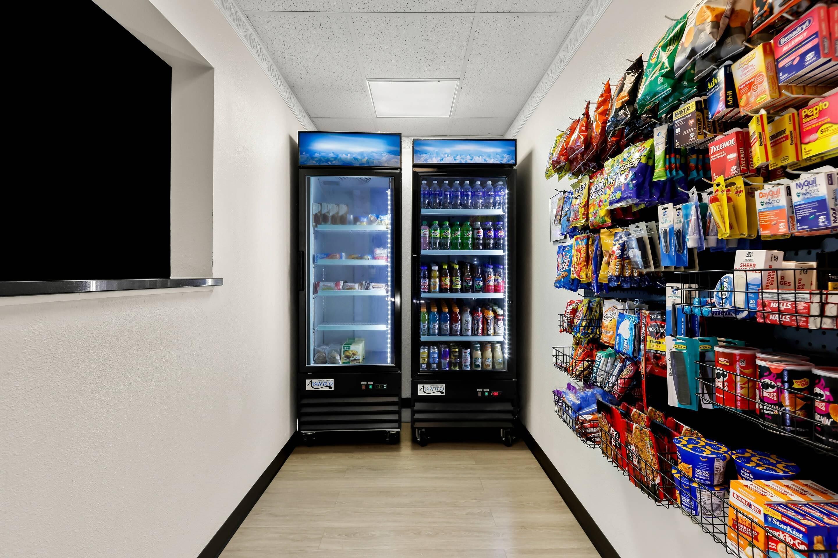 A corridor with two beverage vending machines and shelves stocked with snacks and beverages.