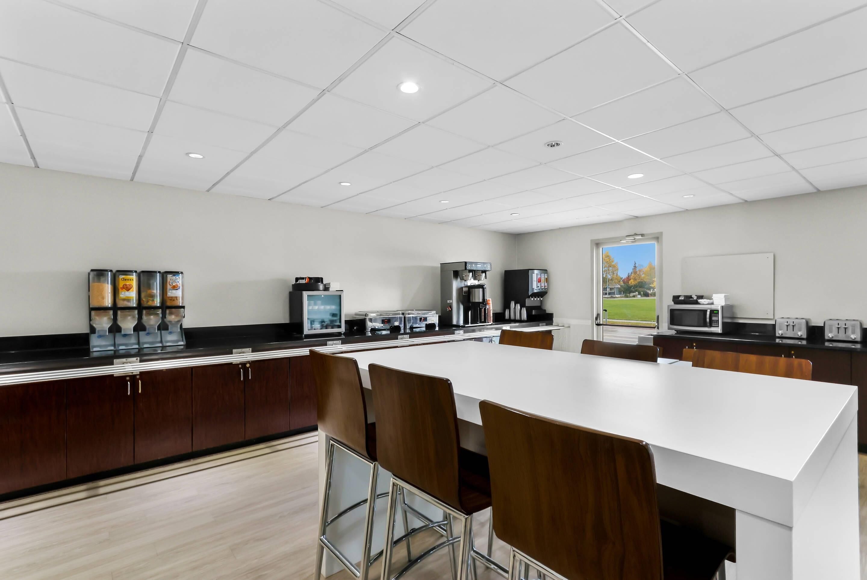 A modern kitchen with a white countertop, stainless steel appliances, and a large window offering a view of the outdoors.