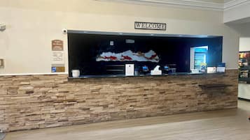 A hotel reception desk with a 'WELCOME' sign, a stone wall, a digital display, and a sign indicating the hotel is smoke-free.