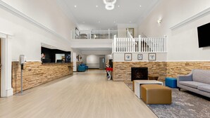 A spacious living area with a wooden accent wall, a fireplace, a sofa, and a staircase to an upper level. - Clarion Suites Anchorage Downtown (Anchorage)