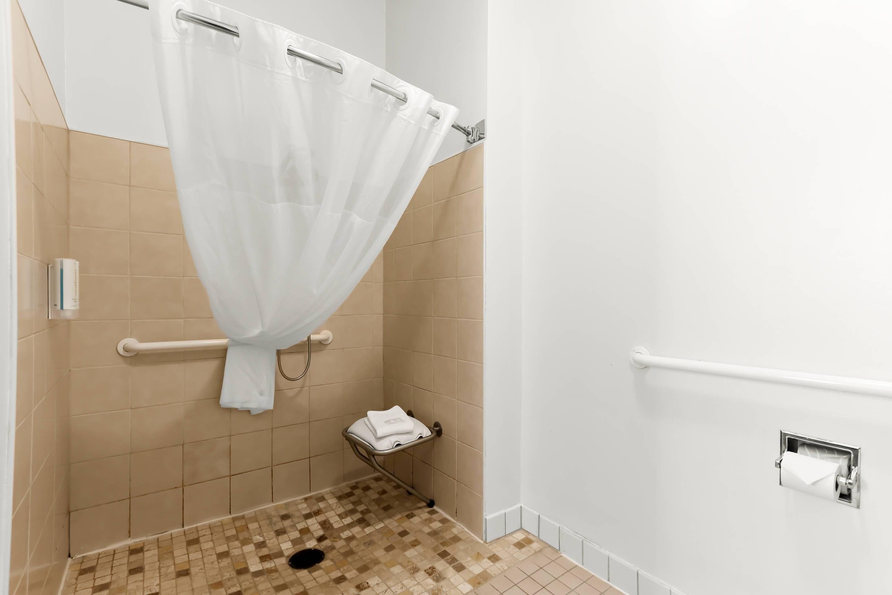 A shower area with a white shower curtain, a grab bar, a towel rack, and a toilet paper holder.