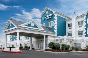 A hotel with a prominent 'Clarion Suites' sign, a covered entrance, and a landscaped area with shrubs. - Clarion Suites Anchorage Downtown (Anchorage)