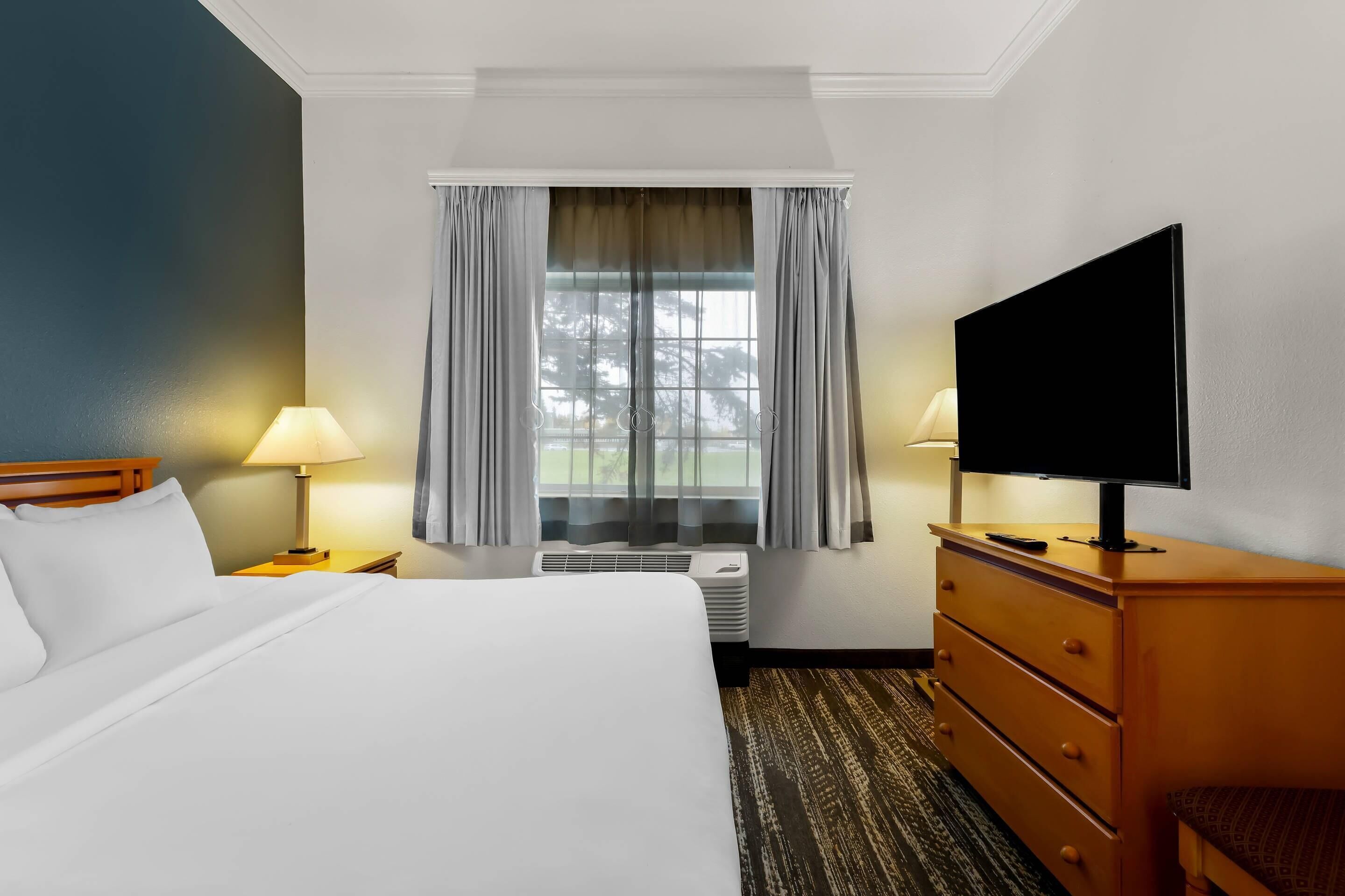 A hotel room with a bed, a television, a dresser, and a window with curtains.