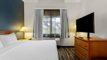 A hotel room with a bed, a television, a dresser, and a window with curtains.