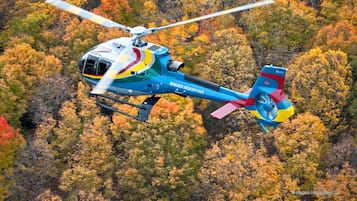 A helicopter with the text "MAGARA HELICOPTERS" flying over a forest with autumn-colored trees.