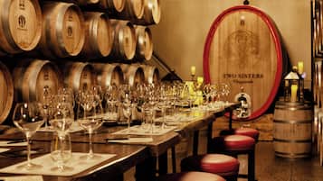 Une salle de dégustation de vins avec des barriques en bois, une grande barrique en bois portant l’inscription « Two Sisters », et de nombreux verres à vin disposés sur une longue table.