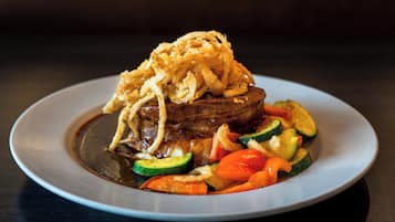 A plate of food with a steak topped with fried onions, accompanied by sliced zucchini, carrots, and bell peppers.