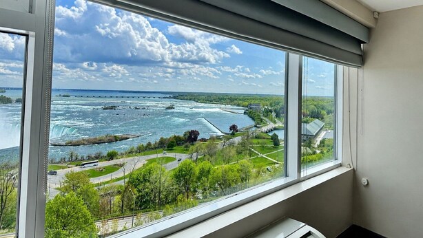 A room with a large window overlooking a river, a bridge, and a park. - Niagara Fallsview Hotel (Niagara Falls)