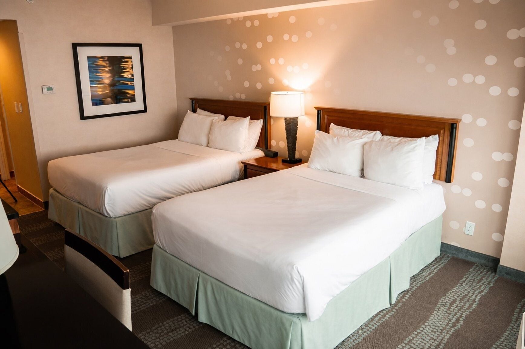 Two twin beds with white linens, a nightstand with a lamp, and a wall with a polka dot pattern.