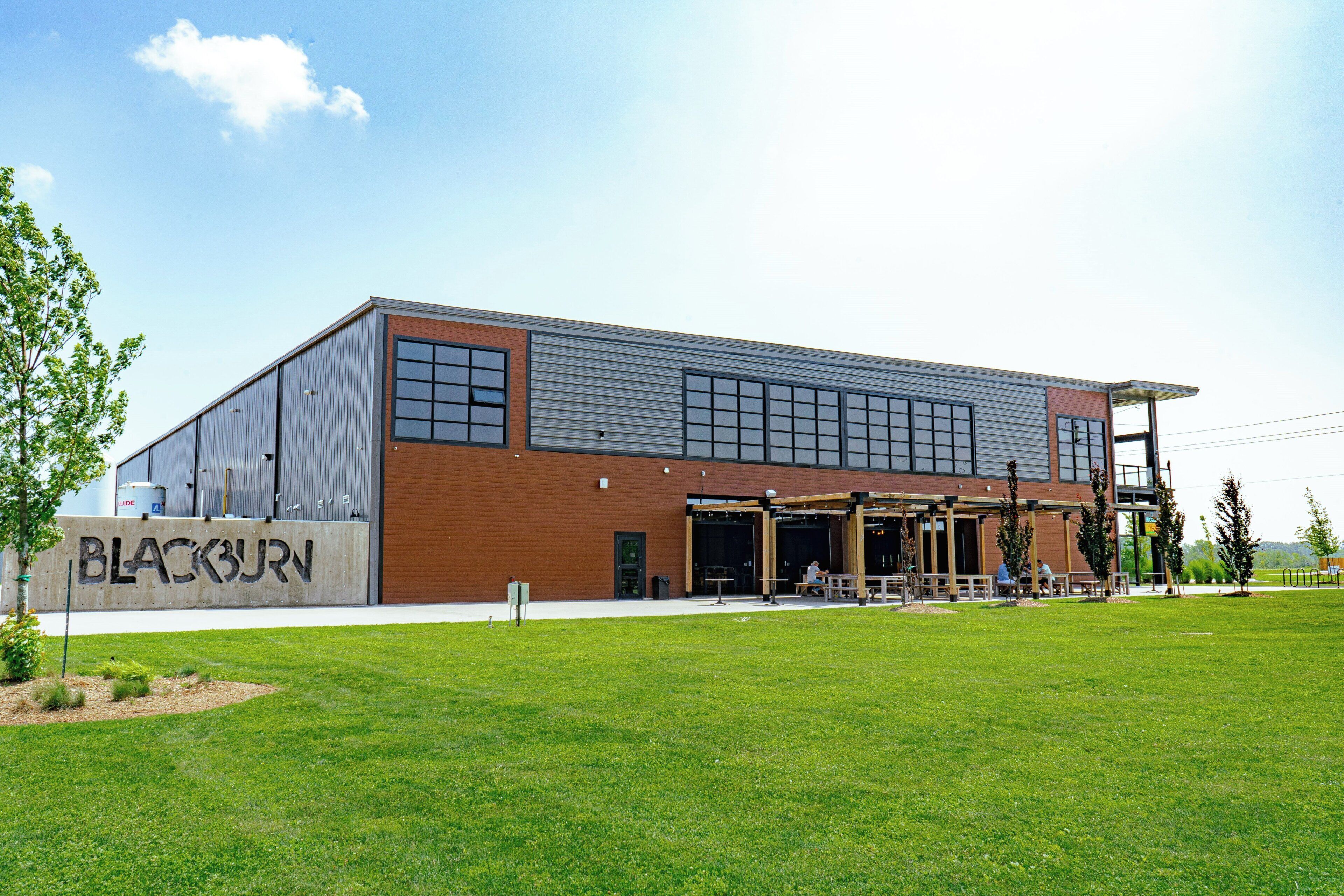 A modern building with a large open entrance, a sign reading 'BLACKBURN,' and a grassy area in front.