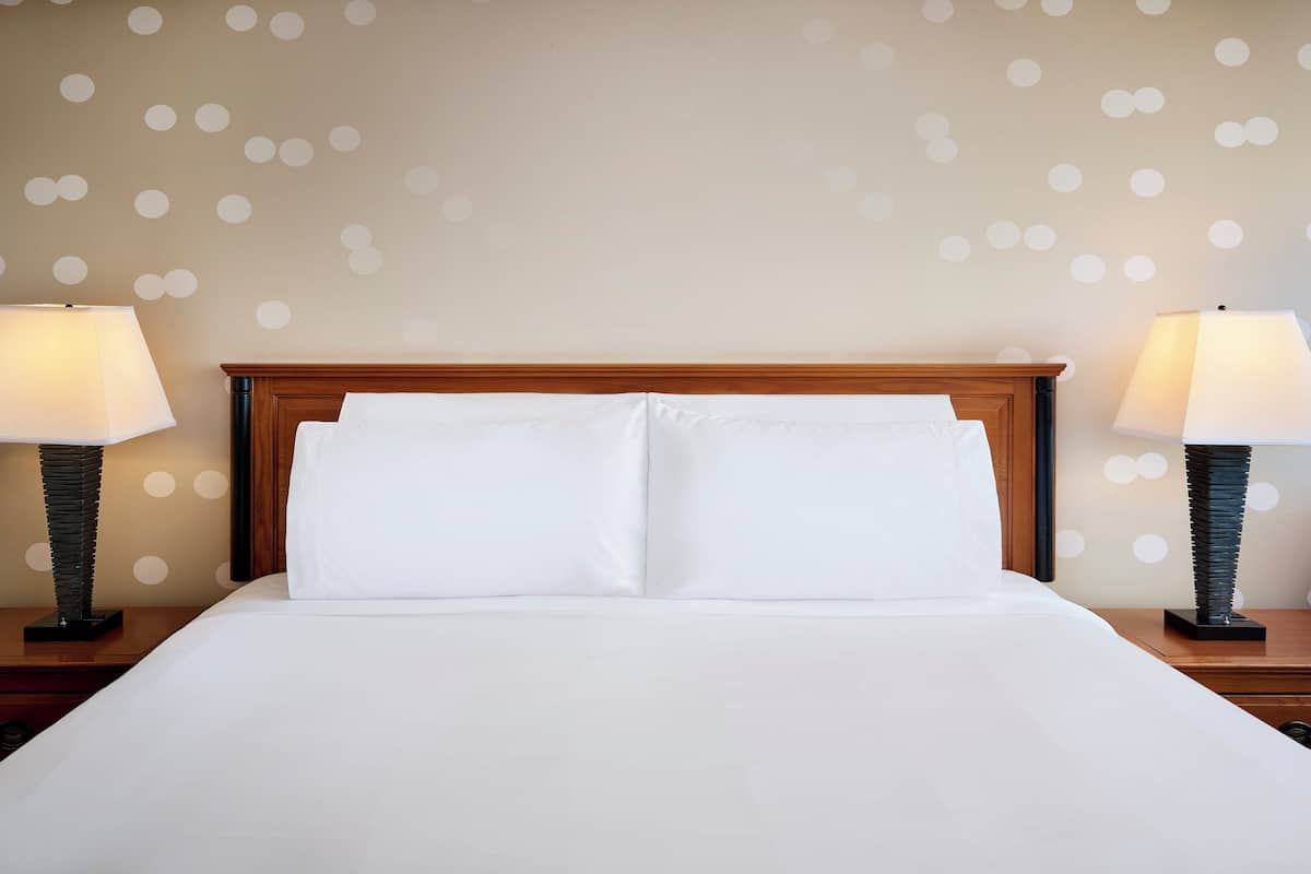 A neatly made bed with white linens, two bedside tables with lamps, and a wall with a polka dot pattern.