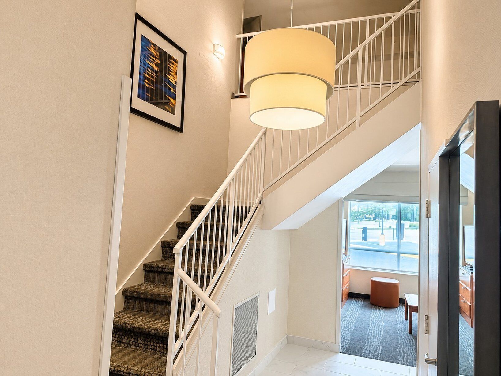 Un escalier avec une rampe blanche, un luminaire suspendu et un tableau encadré au mur.