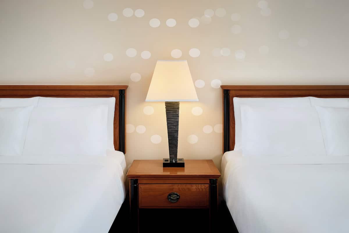 A hotel room with two beds, a nightstand with a lamp, and a wall with circular patterns.