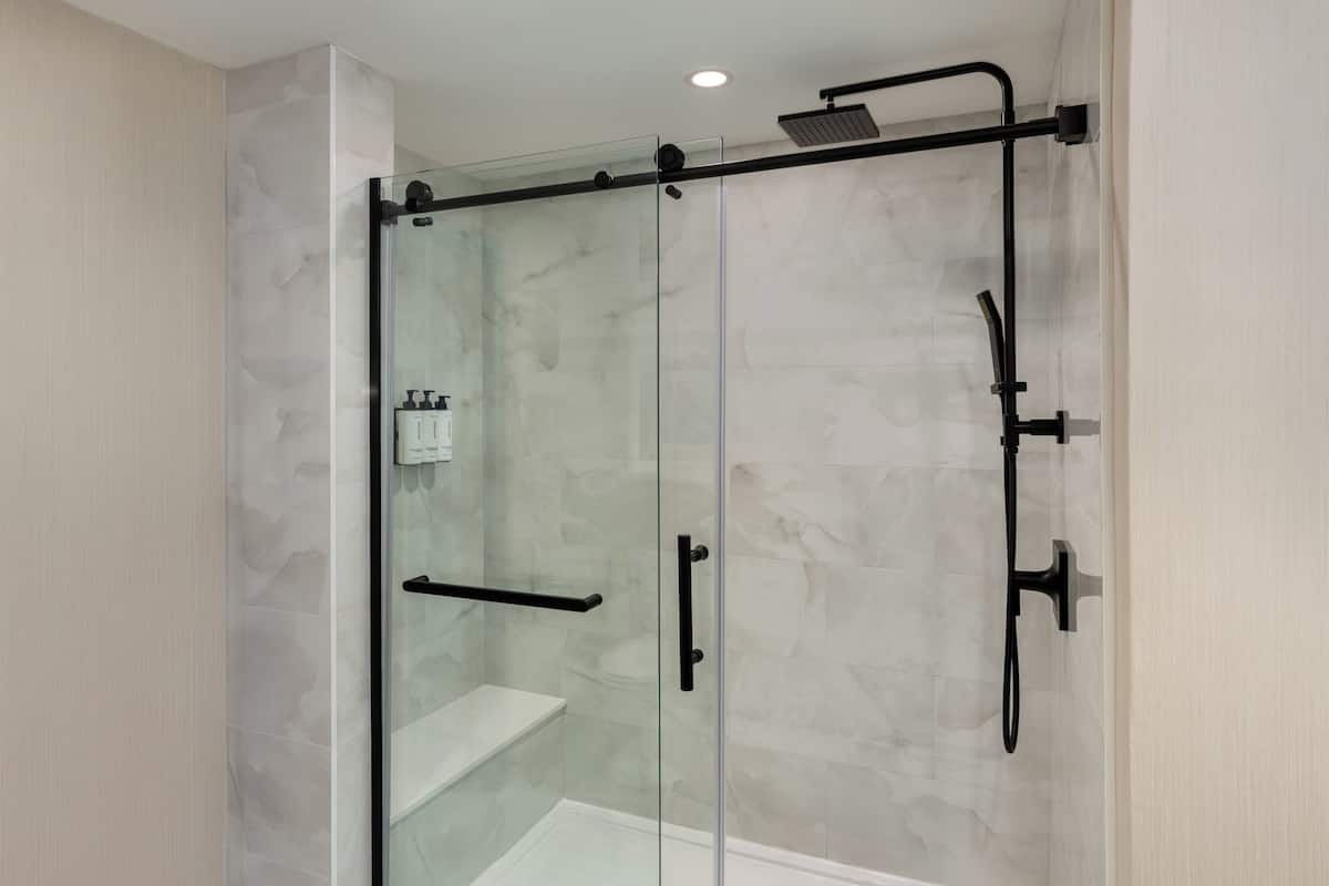 A glass-enclosed shower with a handheld showerhead, a handheld showerhead, and a handheld showerhead.