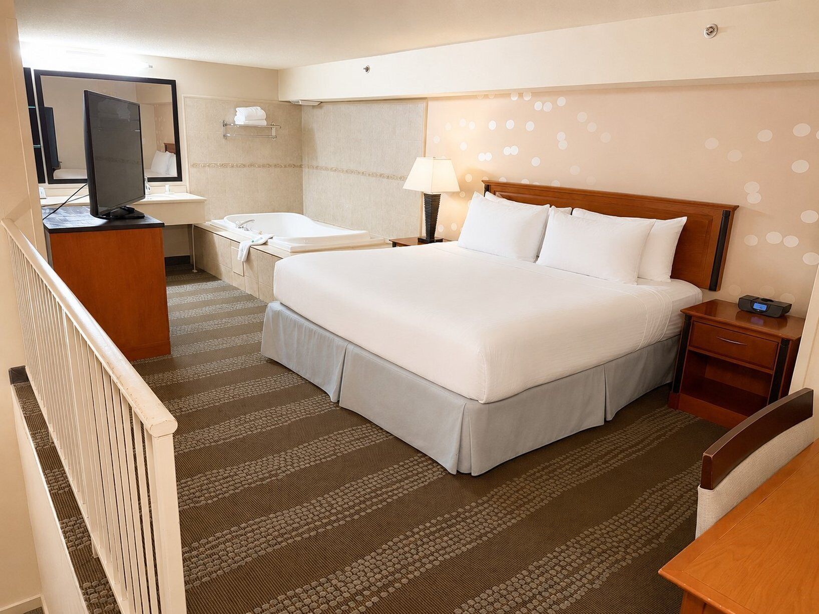 A hotel room with a bed, a desk, a chair, a television, a bathroom, and a patterned carpet.