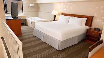 A hotel room with a bed, a desk, a chair, a television, a bathroom, and a patterned carpet.