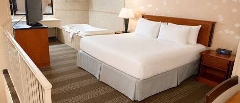 A hotel room with a bed, a desk, a chair, a television, a bathroom, and a patterned carpet.
