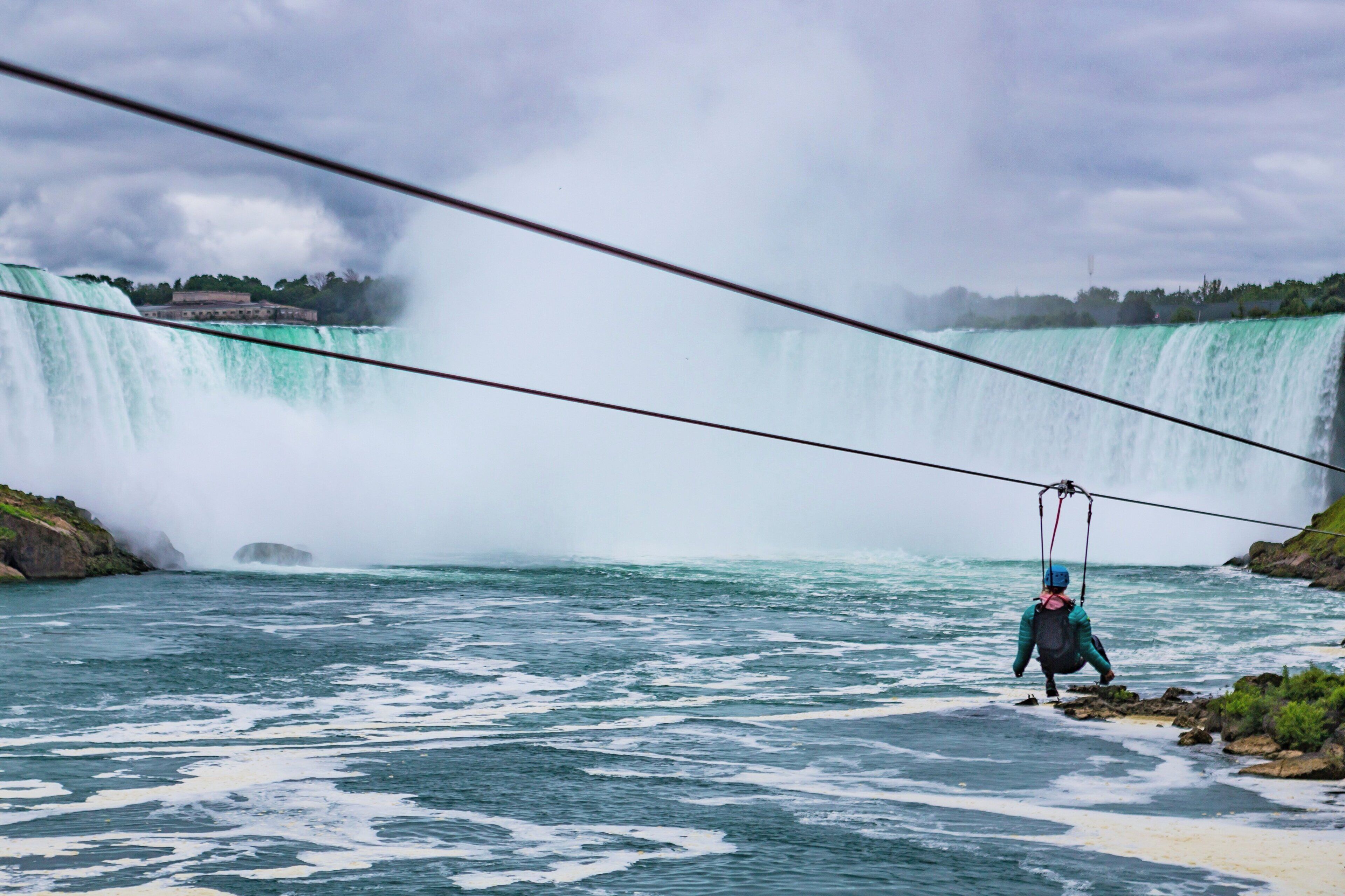 A person on a zip line over a river with a waterfall in the background.