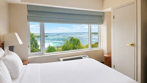 A hotel room with a large window, a bed, a nightstand, a lamp, and a door. - Niagara Fallsview Hotel (Niagara Falls)