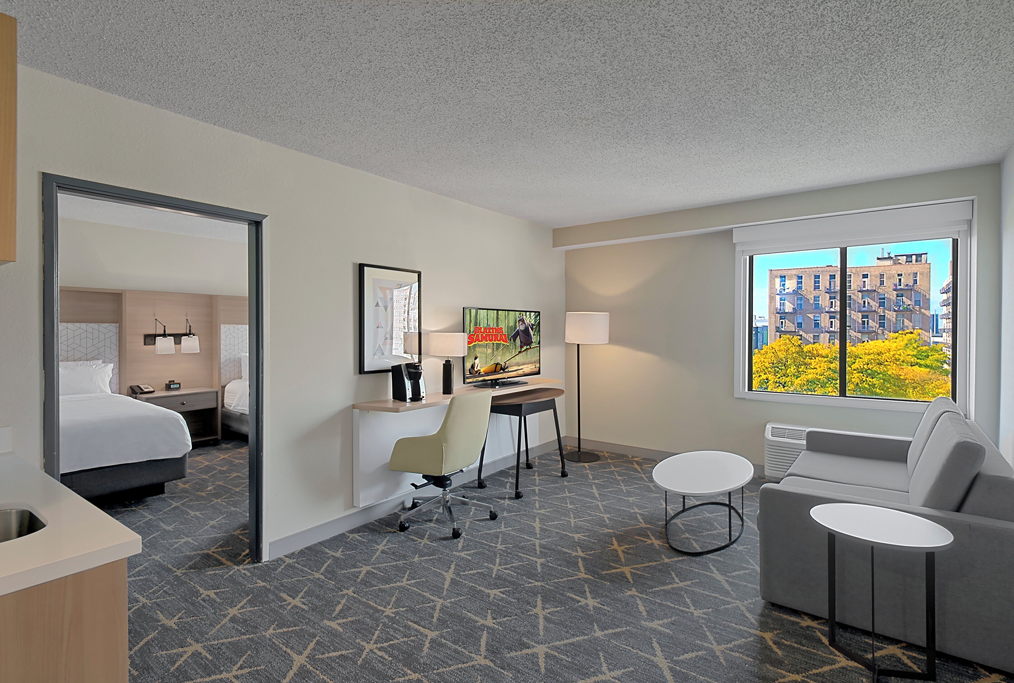 A hotel room with a bed, desk, chair, and a window with a city view.