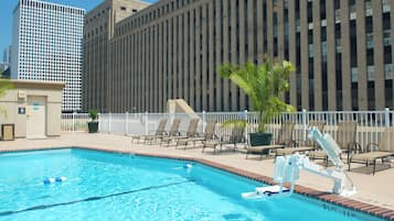 A swimming pool with lounge chairs and a lifeguard chair, surrounded by a fence, with tall buildings in the background.