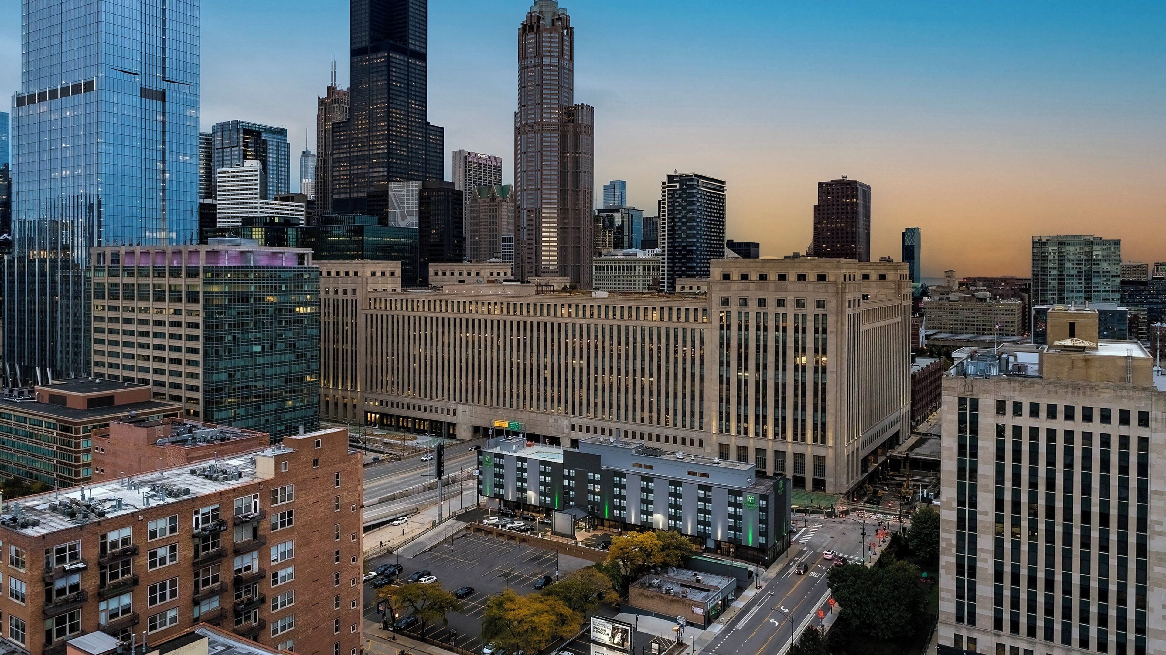 A cityscape with a prominent building featuring a grid-like facade and a parking lot in the foreground.