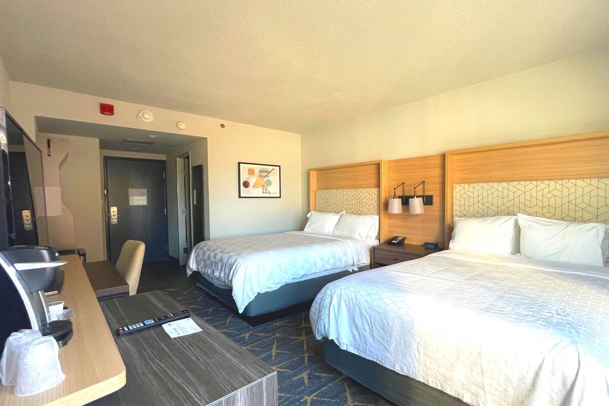 A hotel room with two beds, a desk, a chair, and a small table.