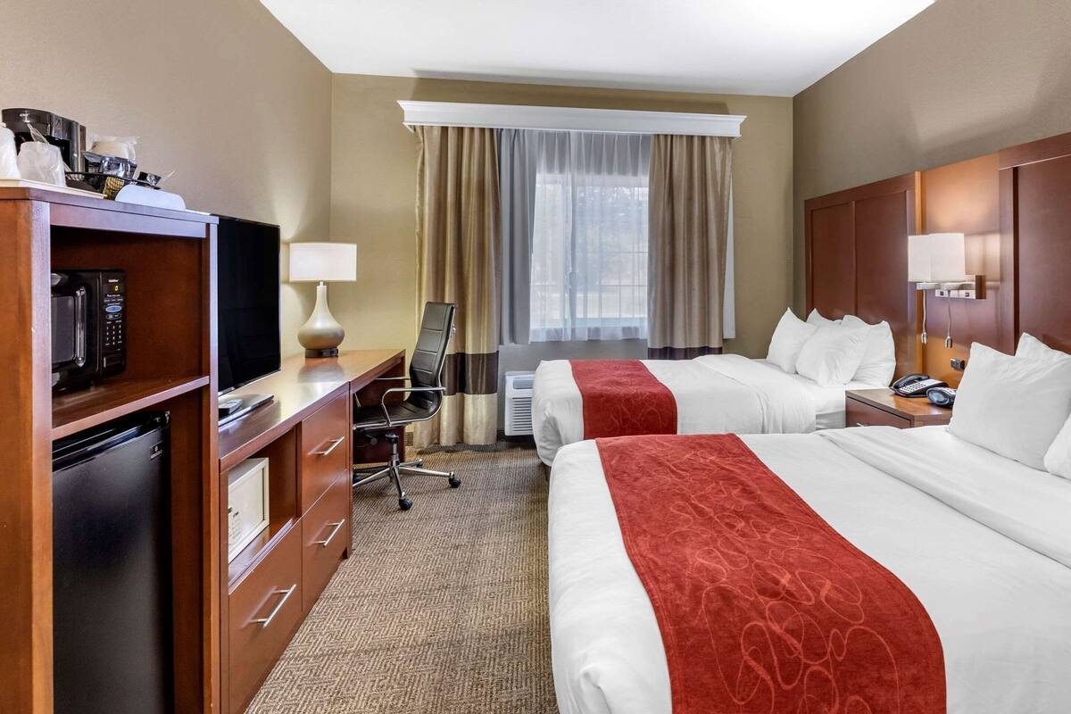 A hotel room with two beds, a desk with a computer, a microwave, and a refrigerator.