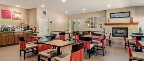 Un restaurant doté de nombreuses tables et chaises, d’un espace cuisine et d’une cheminée.