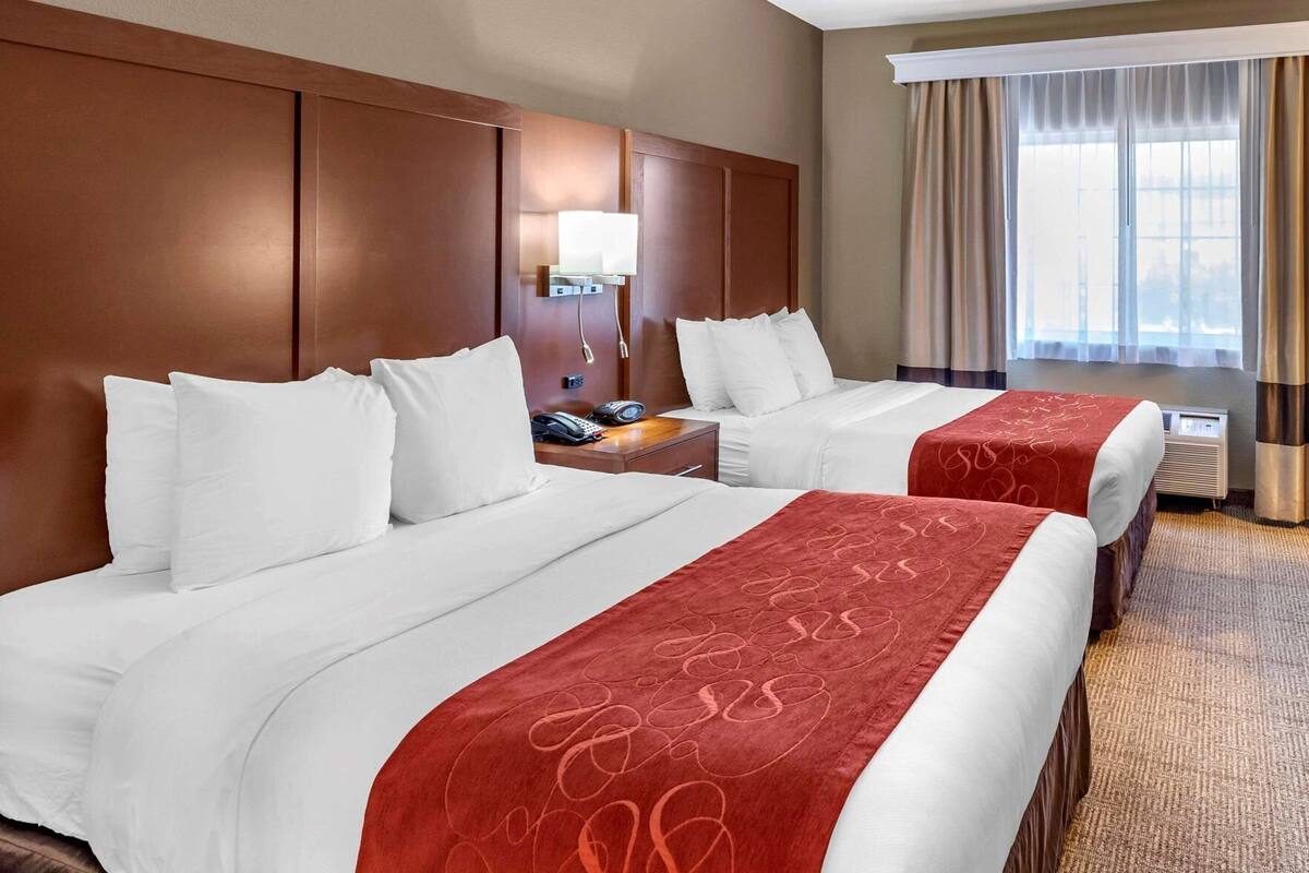 A hotel room with two beds, a nightstand with a phone, a lamp, and a window with curtains.