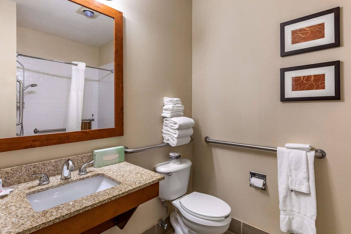 A bathroom with a sink, toilet, and a mirror. There are towels stacked on a rack and two framed pictures on the wall.